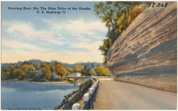 A vintage postcard shows a highway leading into the town of Noel, Missouri.