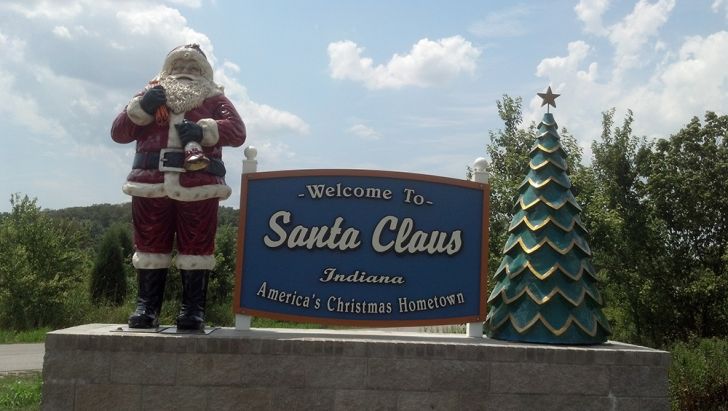 A statue of Santa Claus stands above a ‘Welcome to Santa Claus, Indiana’ sign.