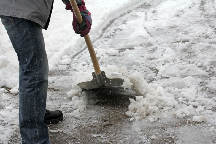 A man shoveling slushy snow in a driveway.