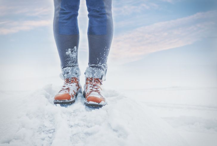 A close-up of a person's legs, feet covered in snow.