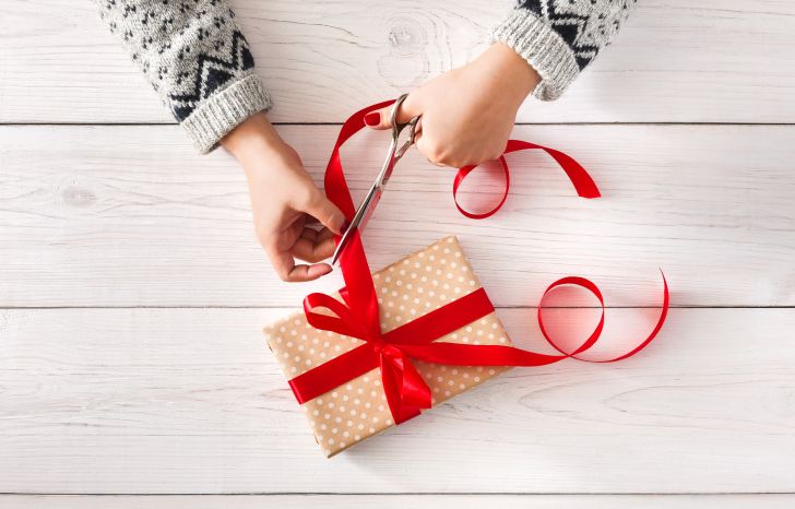 A close up of a person's hands tying a red ribbon around a present.