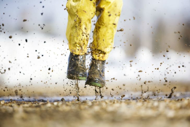 A child in rain boots stomps through the mud