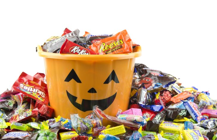 An orange pail with filled with, and surrounded by, Halloween candy.