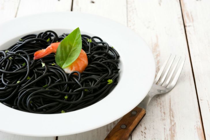 Black pasta is presented on a table