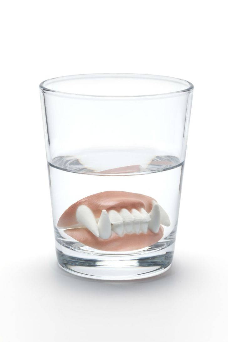 Fake vampire teeth sit at the bottom of a water glass