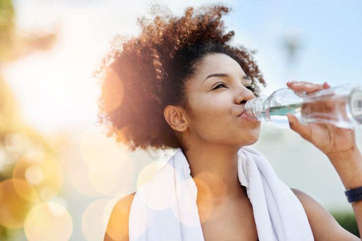 A young woman with a towel around her neck drinking a bottle of water