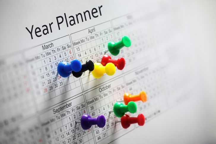 A yearly calendar with several colorful thumbtacks in it