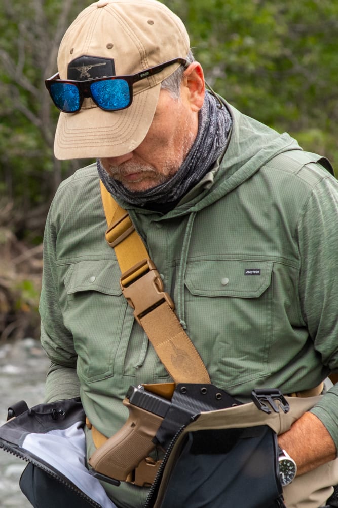 A fly angler wearing a fly fishing technical hoodie and firearm. 