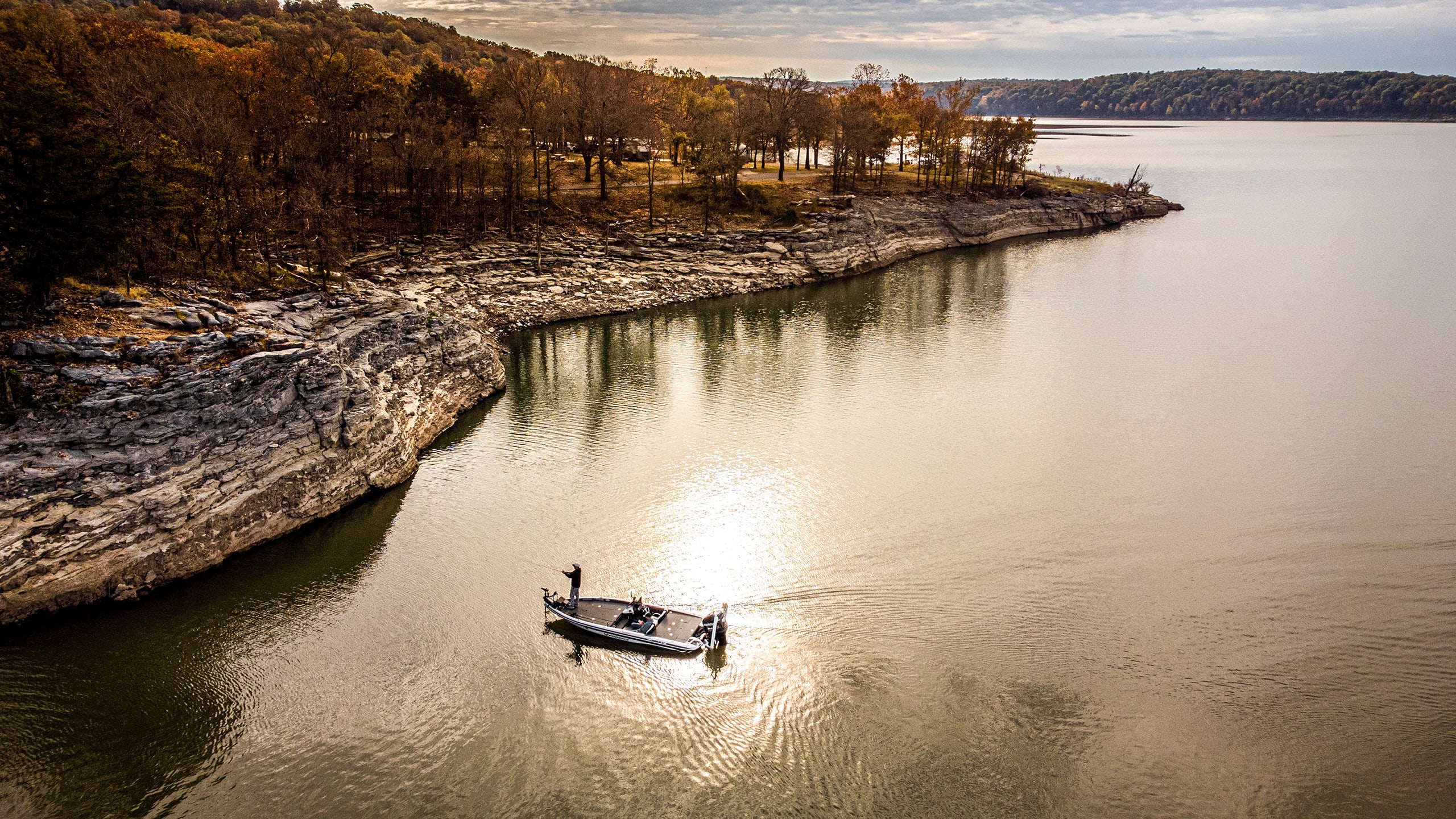 Drone view of a bass boat fishing near a rocky bluff, capturing the calm and tranquil essence of the moment.