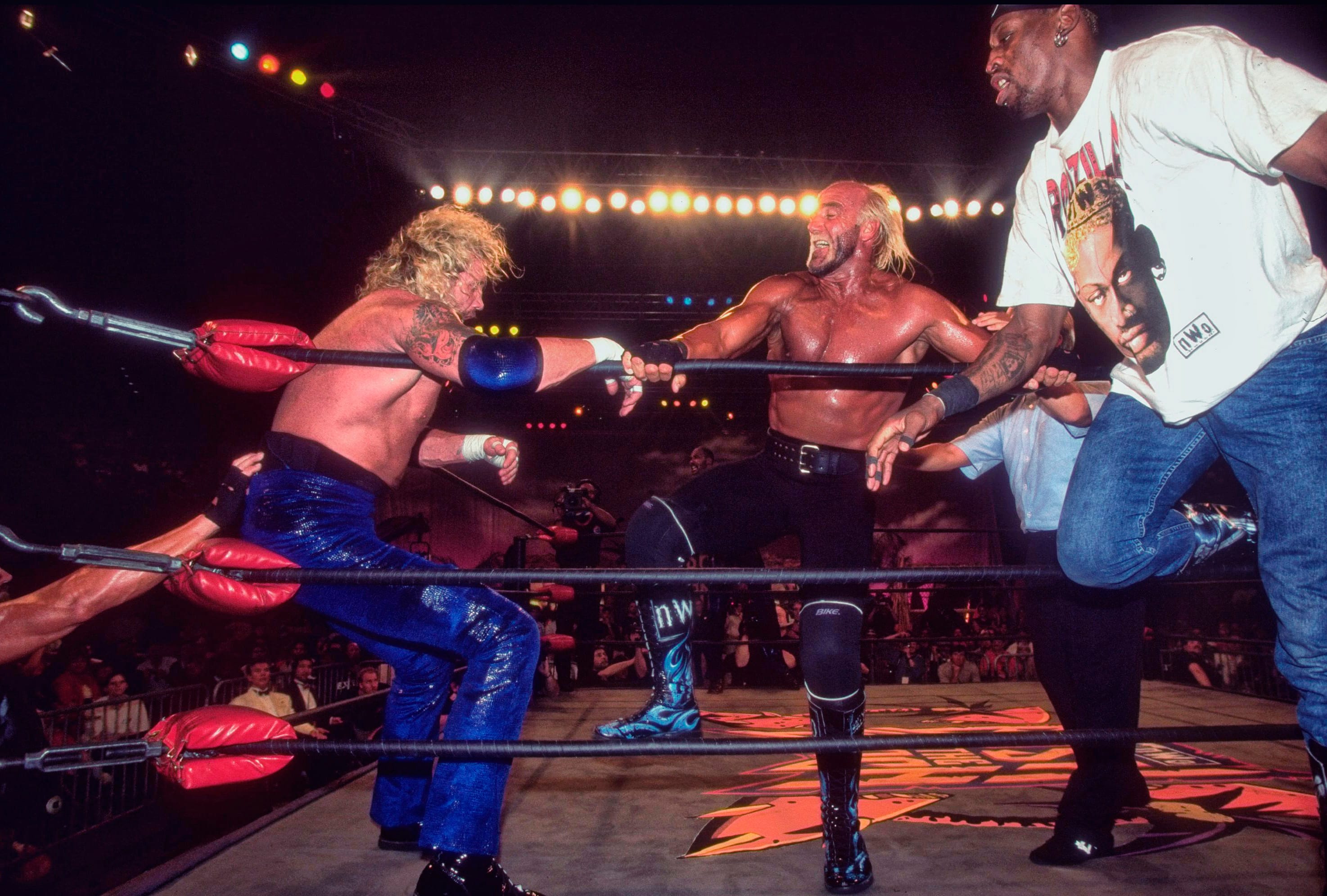 Hulk Hogan lays into Diamond Dallas Page in the corner of the ring while tag team partner Dennis Rodman eggs him on. 