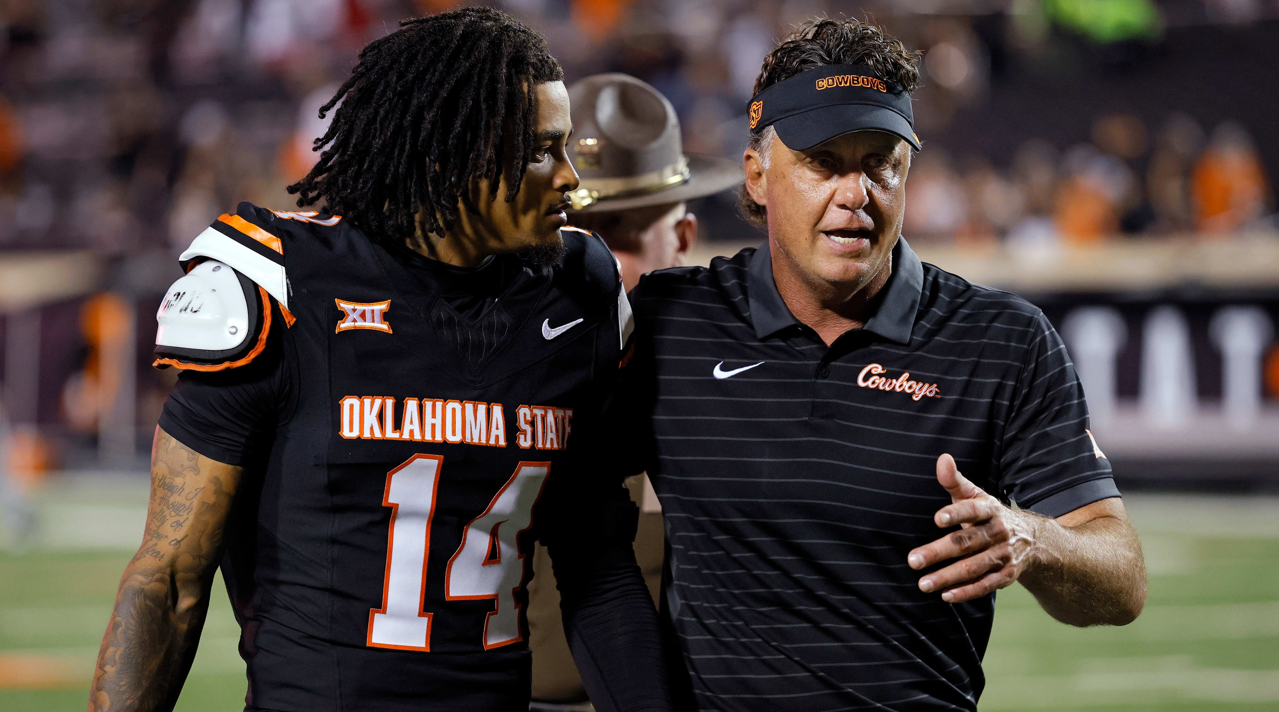 El entrenador en jefe del estado de Oklahoma, Mike Gundi, habló con Landin Cleveland mientras sale al campo.