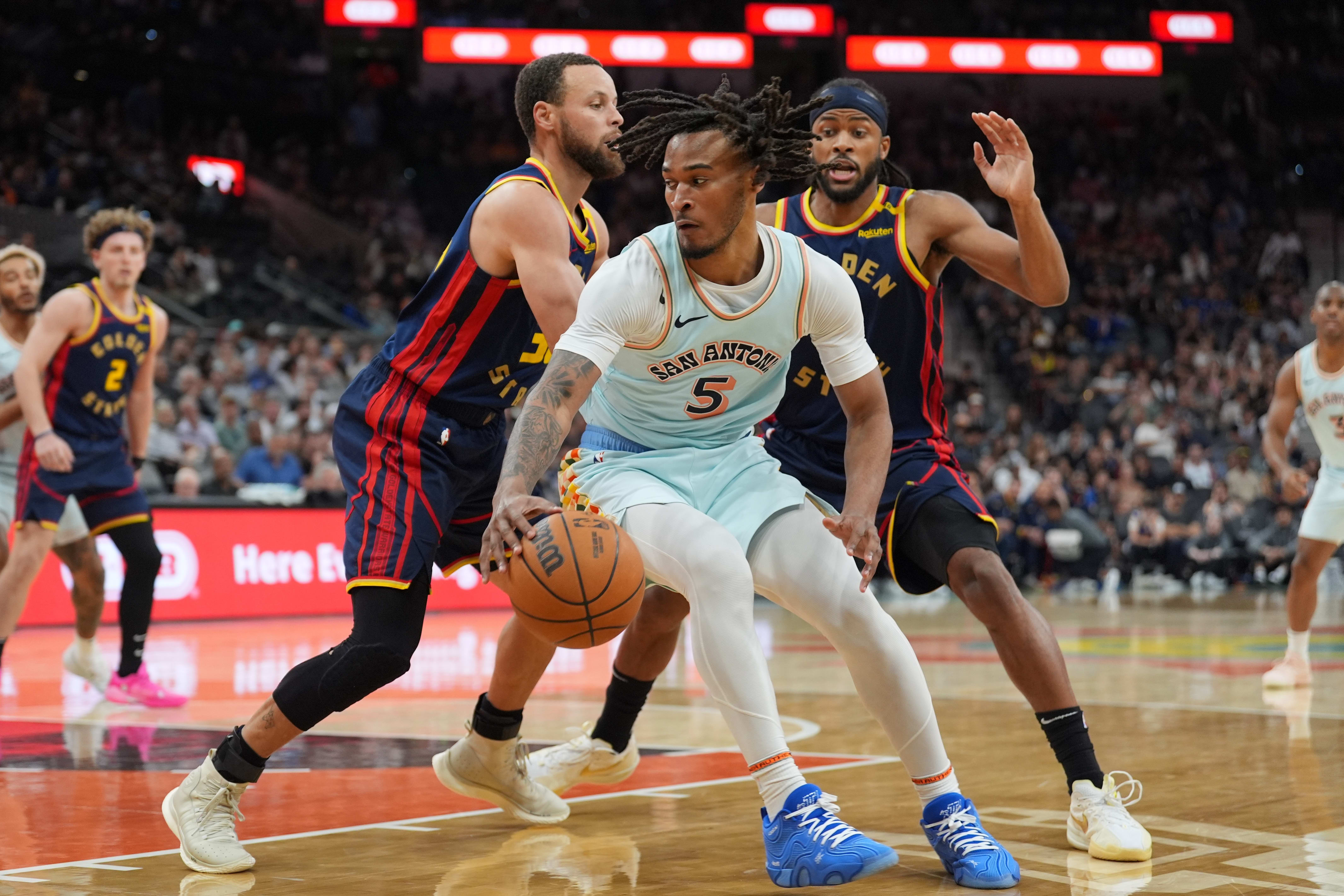 Spurs guard Stephon Castle dribbles in front of Warriors guards Stephen Curry and Buddy Hield.
