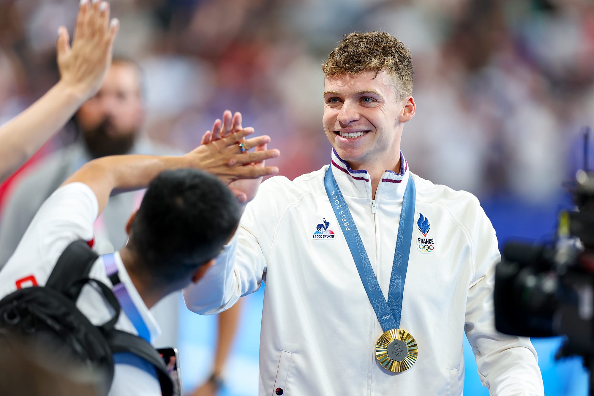Leon Marchand high fives fans after receiving a gold medal at the Paris Olympics
