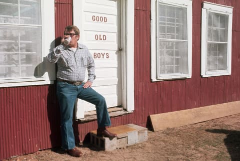 Billy Carter enjoying a beer (possibly a Billy Beer?) in front of a men's room.