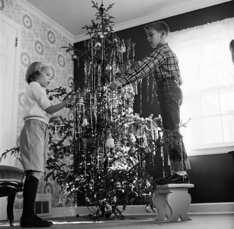 Children putting tinsel on a Christmas tree circa 1955.