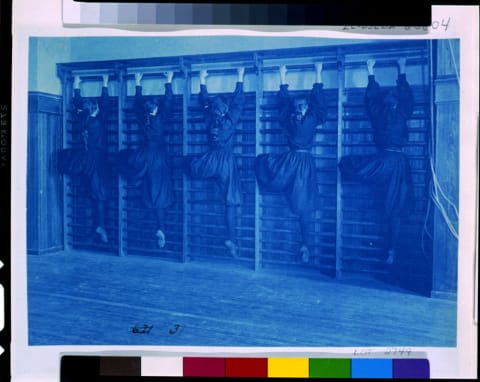 Girls in bloomers on climbing apparatus.