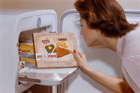 A woman taking a Swanson TV dinner from the freezer.