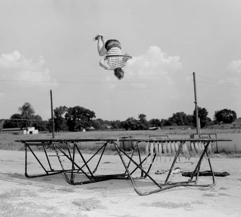 A boy wearing a hula hoop jumps on a trampoline, ca. 1955.