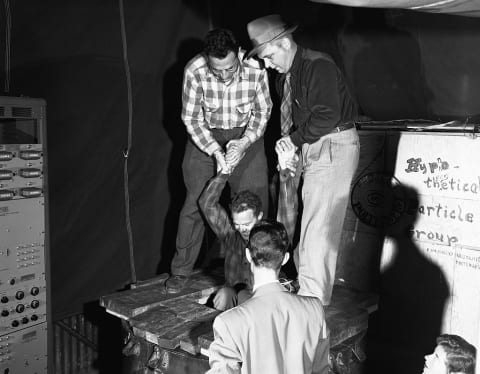 Fred Reines (left) and Clyde Cowan (in hat) demonstrate their methods in searching for the existence of the neutrino, using one of their colleagues.