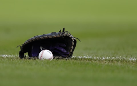 A ball and glove lays on the field at the beginning of a game between the Reds and Rockies.