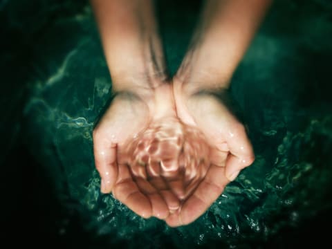 A person cups the palms of their hands to catch water.