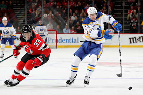 NEWARK, NEW JERSEY – APRIL 21: Dylan Cozens #24 of the Buffalo Sabres steals the puck from Ryan Graves #33 of the New Jersey Devils during the third period at Prudential Center on April 21, 2022 in Newark, New Jersey. The Buffalo Sabres defeated the New Jersey Devils 5-2. (Photo by Elsa/Getty Images)