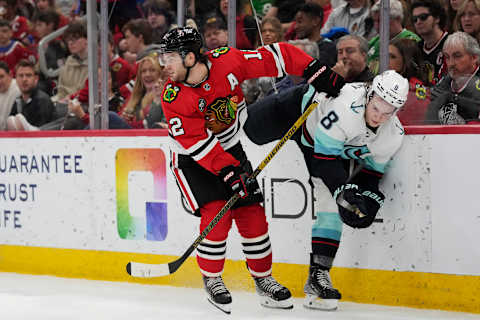 CHICAGO, ILLINOIS – APRIL 07: Alex DeBrincat #12 of the Chicago Blackhawks checks Cale Fleury #8 of the Seattle Kraken into the boards during the second period at United Center on April 07, 2022 in Chicago, Illinois. (Photo by Patrick McDermott/Getty Images)