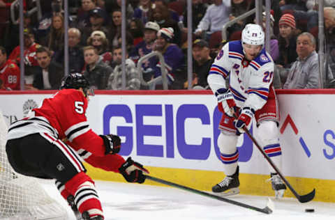 CHICAGO, ILLINOIS – DECEMBER 07: Dryden Hunt #29 of the New York Rangers tries to push the puck away from Ian Mitchell #51 of the Chicago Blackhawks at the United Center on December 07, 2021 in Chicago, Illinois. The Rangers defeated the Blackhawks 6-2. (Photo by Jonathan Daniel/Getty Images)