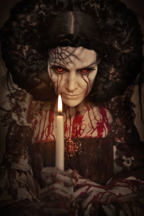 A scary-looking woman covered in blood with a glowing candle in front of her