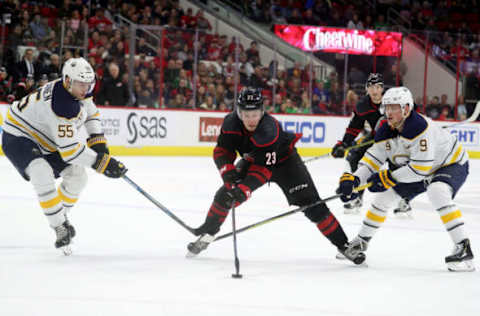 RALEIGH, NC – MARCH 16: Brock McGinn #23 of the Carolina Hurricanes controls the puck through the defense of Rasmus Ristolainen #55 of the Buffalo Sabres and Jack Eichel #9 during an NHL game on March 16, 2019 at PNC Arena in Raleigh, North Carolina. (Photo by Gregg Forwerck/NHLI via Getty Images)