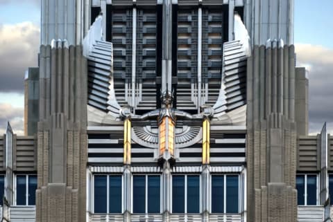 A stainless steel Art Deco winged sculpture on the facade of an embellished building.