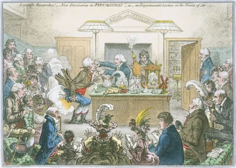 A 19th-century illustration satirizes Humphry Davy's experiments with nitrous oxide. Davy operates the bellows filled with laughing gas, which flows through a tube in his assistant's mouth, resulting in the gas exploding out of his bum.