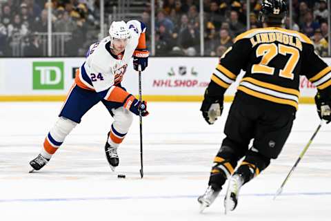 BOSTON, MASSACHUSETTS – DECEMBER 13: Scott Mayfield #24 of the New York Islanders skates the puck against Hampus Lindholm #27 of the Boston Bruins during an overtime period at the TD Garden on December 13, 2022, in Boston, Massachusetts. (Photo by Brian Fluharty/Getty Images)