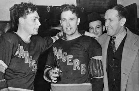 (Original Caption) This is a group of victorious Rangers in their dressing room after the New York Hockey team won their first Stanley Cup championship in seven years at Toronto. Bryan Hextall, (L), slammed in the winning score in an overtime period, to win for the rangers 3-2, over the Toronto Maple Leafs. In the center is Goalie Kerr, and at right is Coach Frank Boucher.