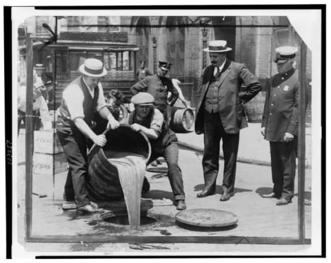 New York City Deputy Police Commissioner John A. Leach (right) watches agents pour liquor into sewer following a raid during the height of Prohibition.