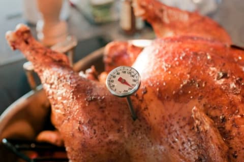 A turkey out of the oven with a thermometer sticking out of it.