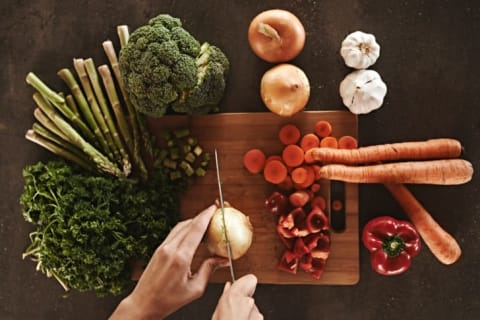 A person slicing an onion and other vegetables.