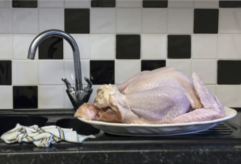 Raw turkey on a platter next to a sink.