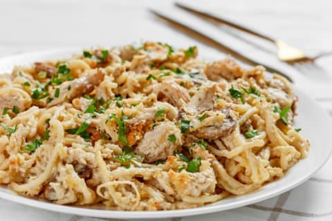 close-up of roasted turkey breast tetrazzini served on a white plate with golden fork and knife on a wooden table