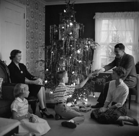 A family around a lighted Christmas tree, circa 1955.