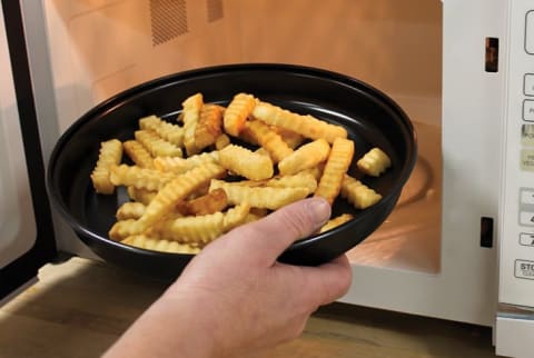 A man puts french fries in the microwave on a crisper tray.