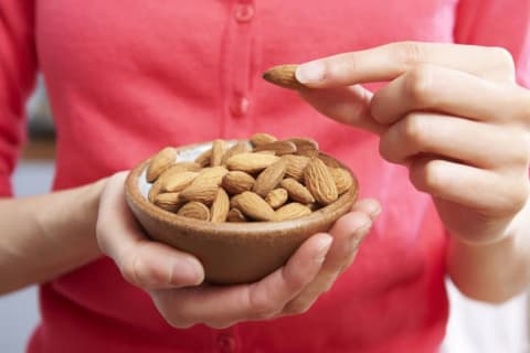 A woman picks up an almond from a bowl.