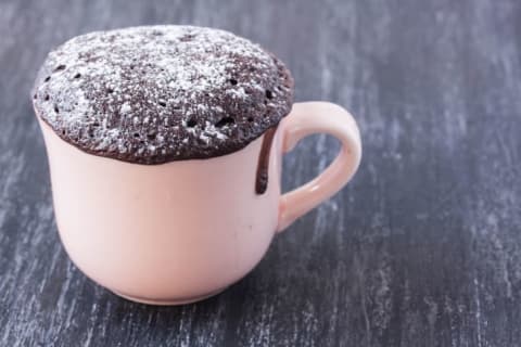 A chocolate cake dusted with powdered sugar in a white mug