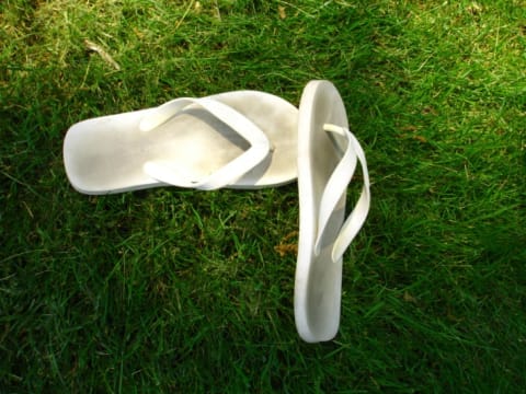 A pair of really dirty white flip-flops sitting on top of very green grass