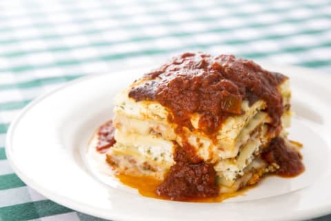 Lasagna with meat sauce sitting on a white plate on top of a green checkered tablecloth