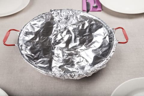 A round dish covered in foil sits on a table.