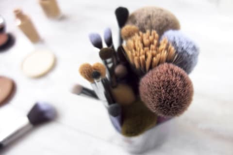 A cup full of makeup brushes of various shapes and sizes sitting on a white countertop.