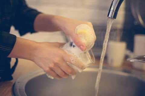 Female hands washing a clear glass under a stream of water in a sink