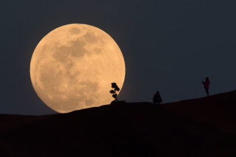 A person poses for a photo as the moon rises over Griffith Park in Los Angeles, California, on January 30, 2018.