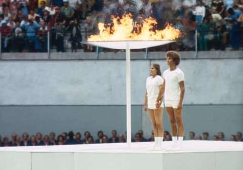 Two teens stand next to the Olympic cauldron.